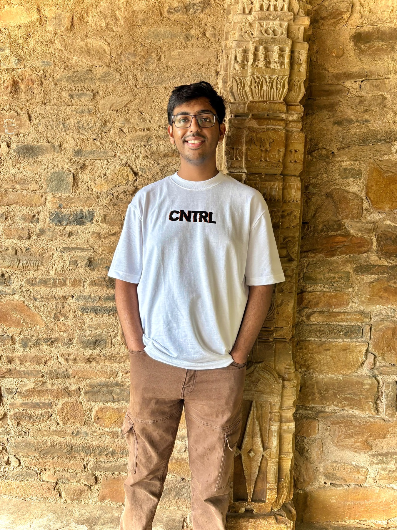 Harshit smiling in front of a warm stone wall